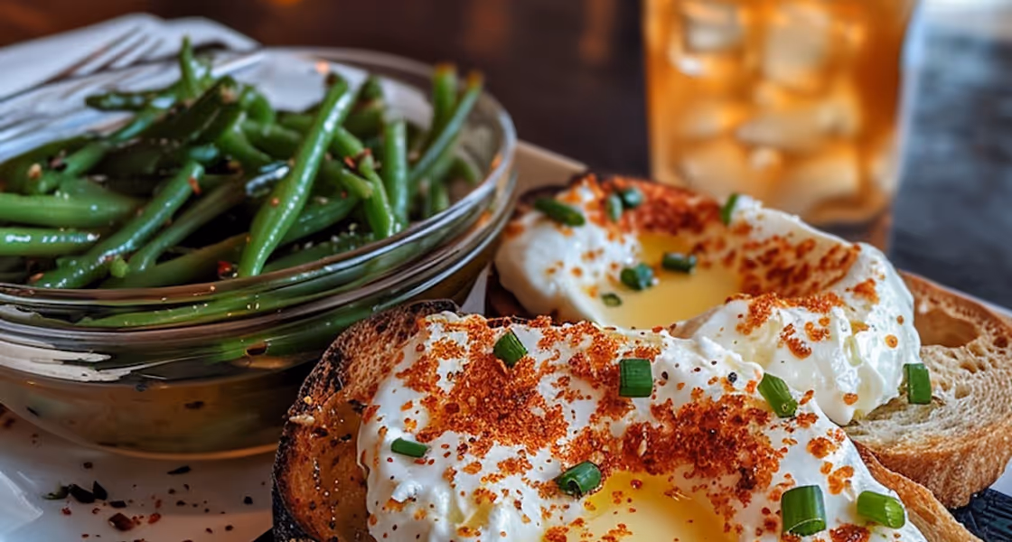 Two slices of toasted bread topped with whipped cream cheese, sprinkled with red seasoning and chopped green onions, served with a bowl of seasoned green beans and a glass of iced tea.